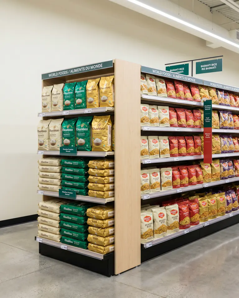 Khushboo basmati and Bikaneri Bites in retail-ready facing on a Canadian world-foods shelf — Loblaws/Save-On aesthetic.